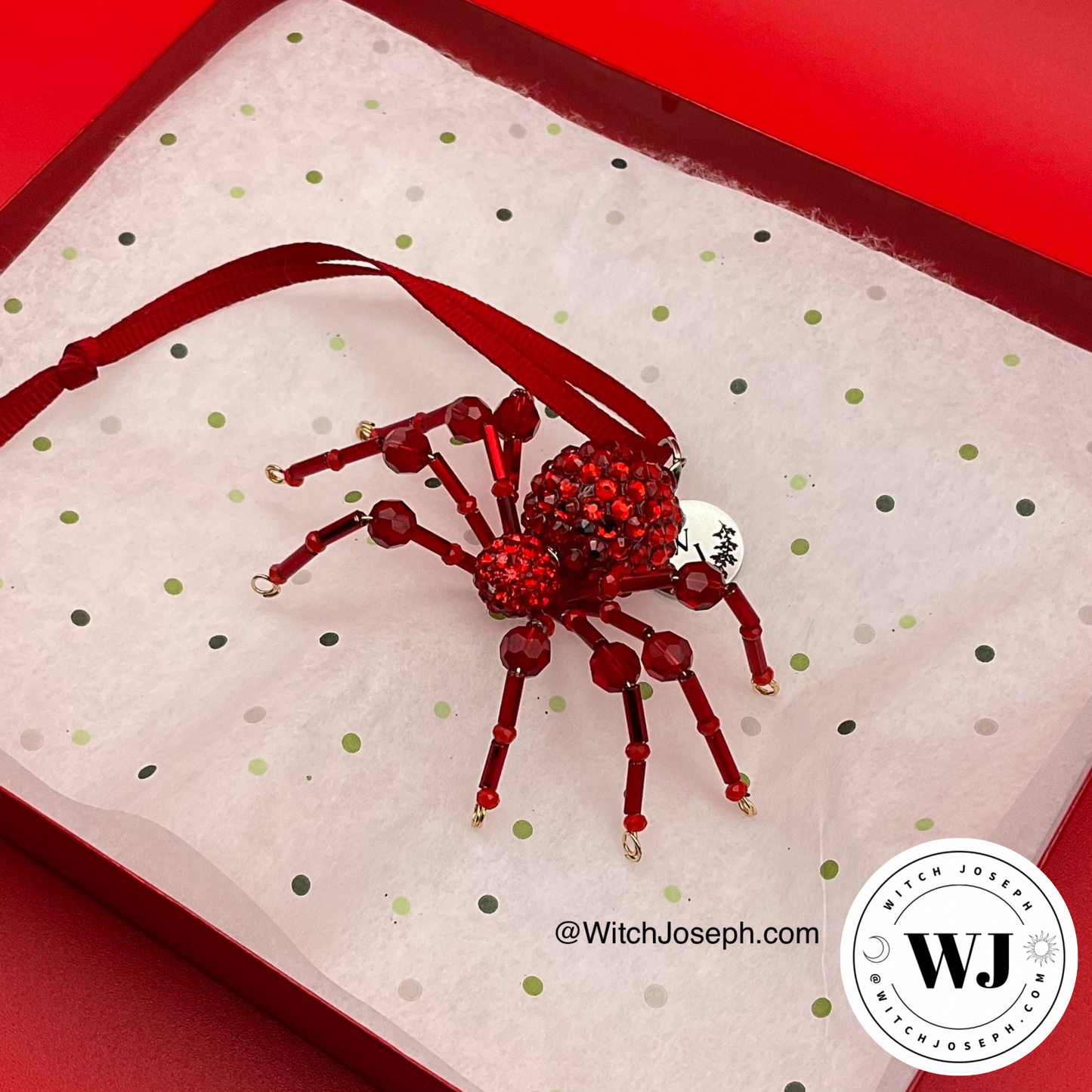 Red spider ornament in it’s holiday box on a red background with the Witch Joseph logo