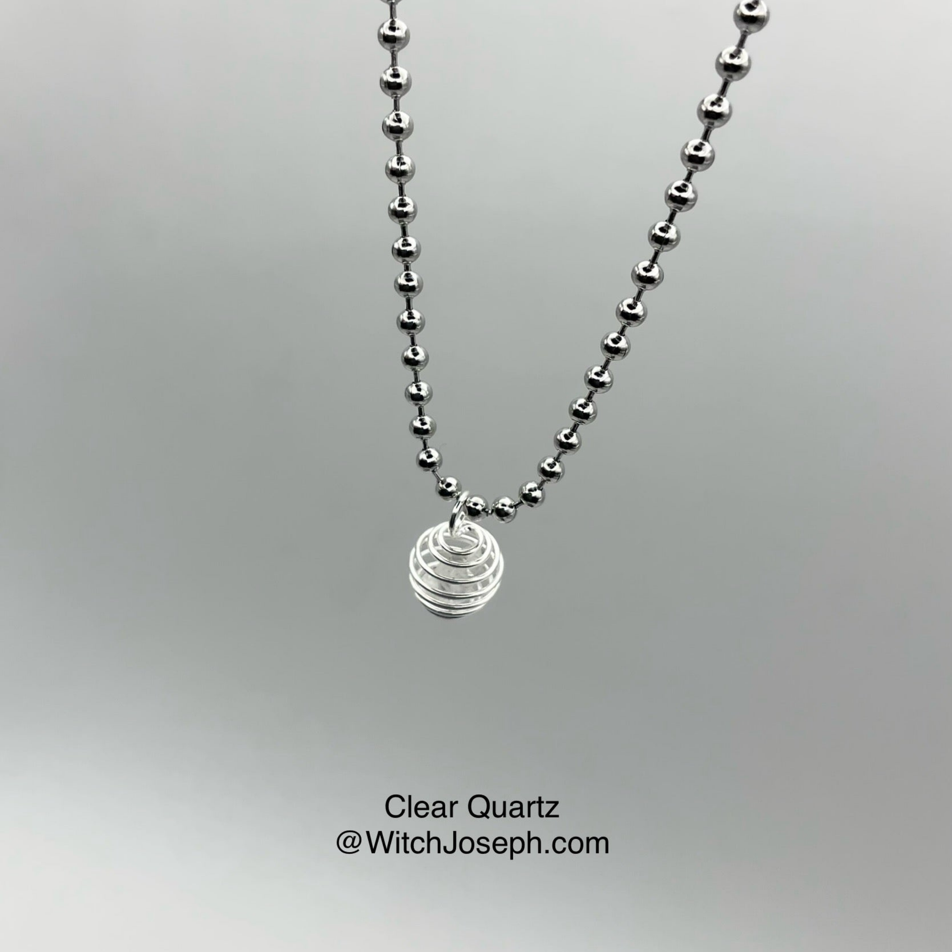 Silver tone ball chain necklace with a clear quartz chip in cage pendant on a gray background
