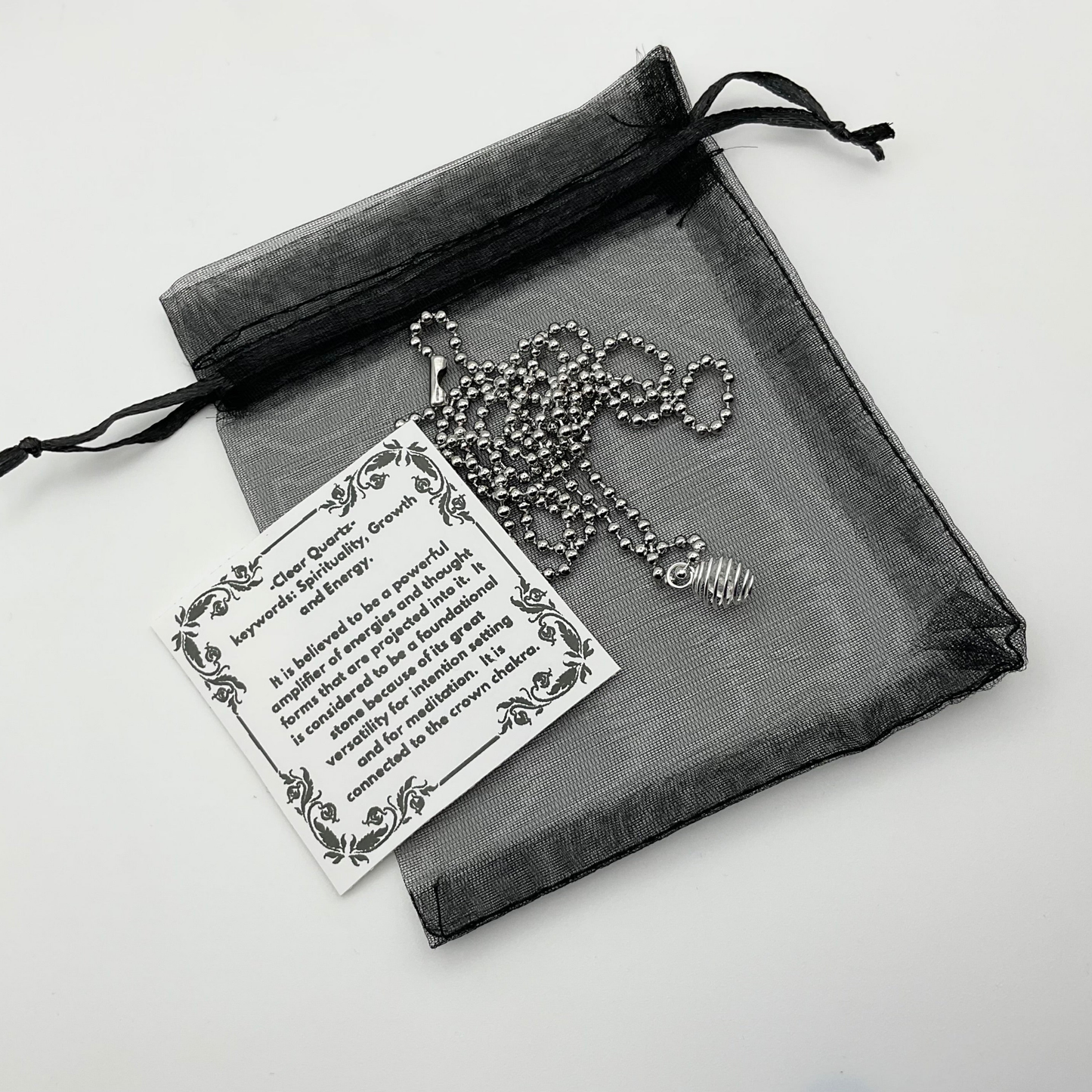 Necklace with quartz chip cage pendant and card on a sheer black bag