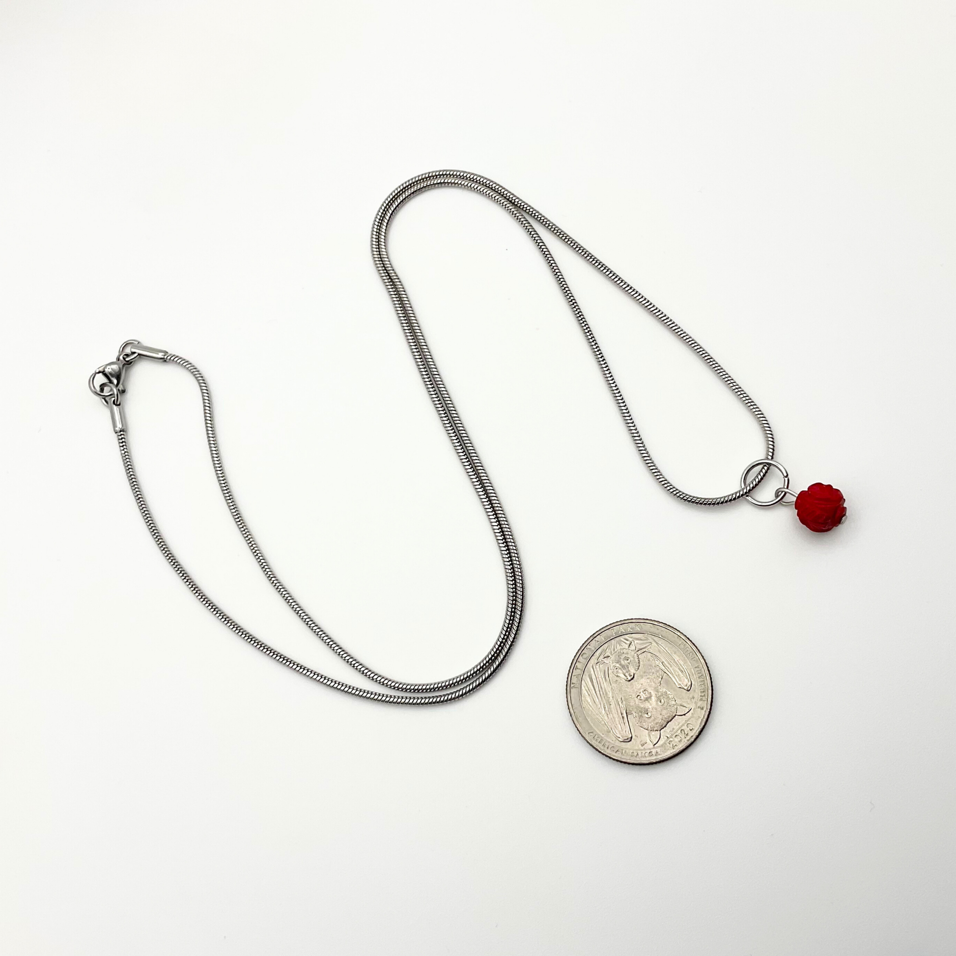 Silver tone necklace with a red coral pendant next to a coin on a white background