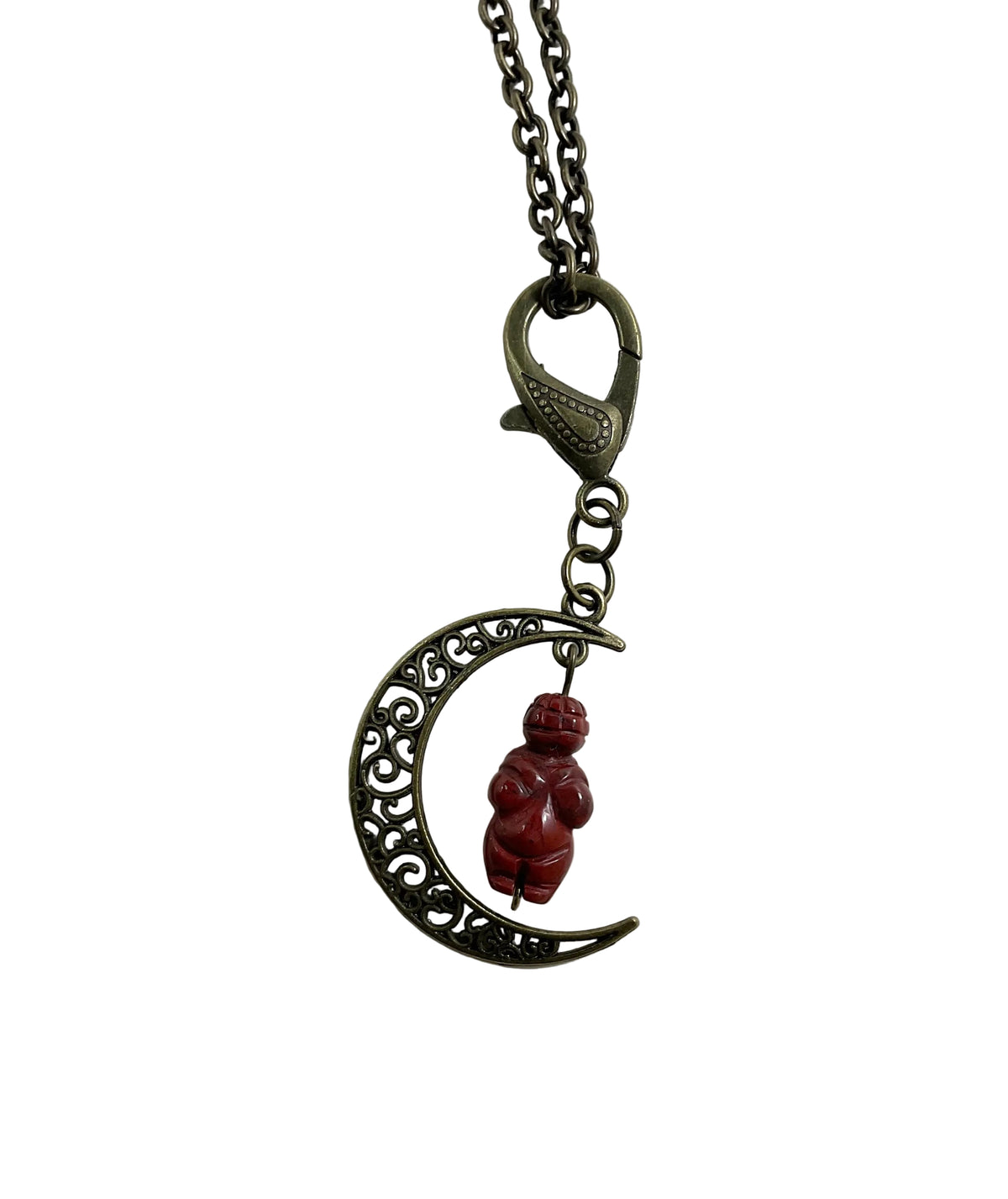 A metal pendant necklace featuring a crescent moon with ornate filigree detailing and a small red jasper Goddess carved figurine hanging in the center, suspended from a chain with a lobster clasp, shown on a plain white background.