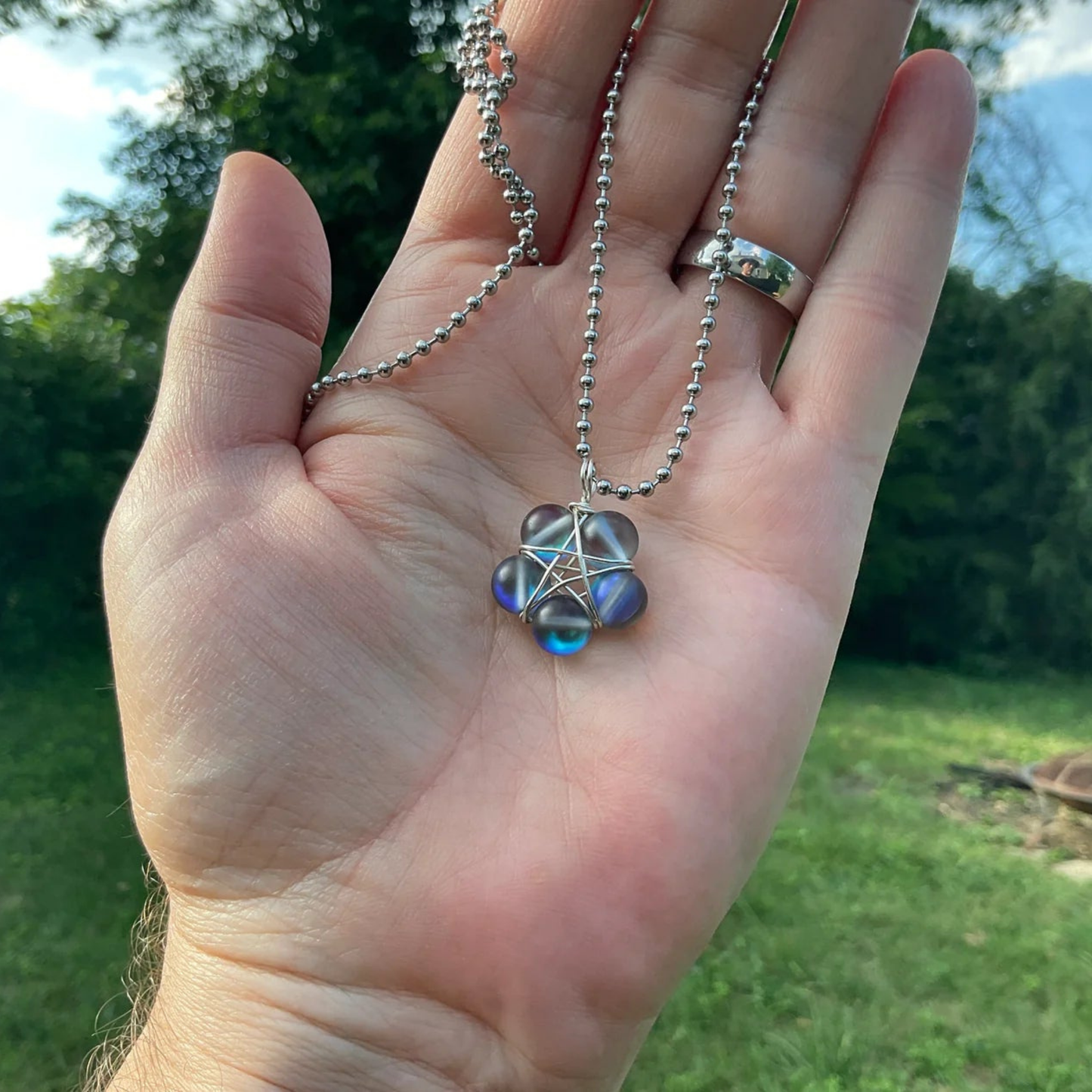 Hand holding a necklace with a pentagram pendant against a natural garden background