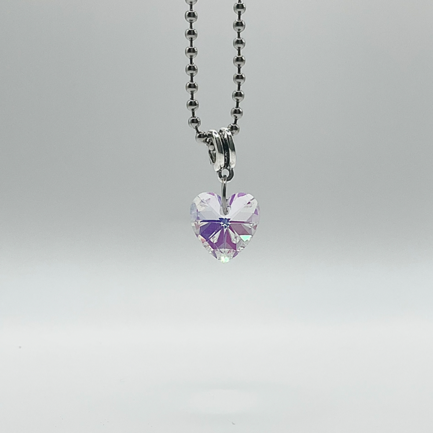 Sparkling Heart-shaped crystal pendant on a ball chain against a gray background