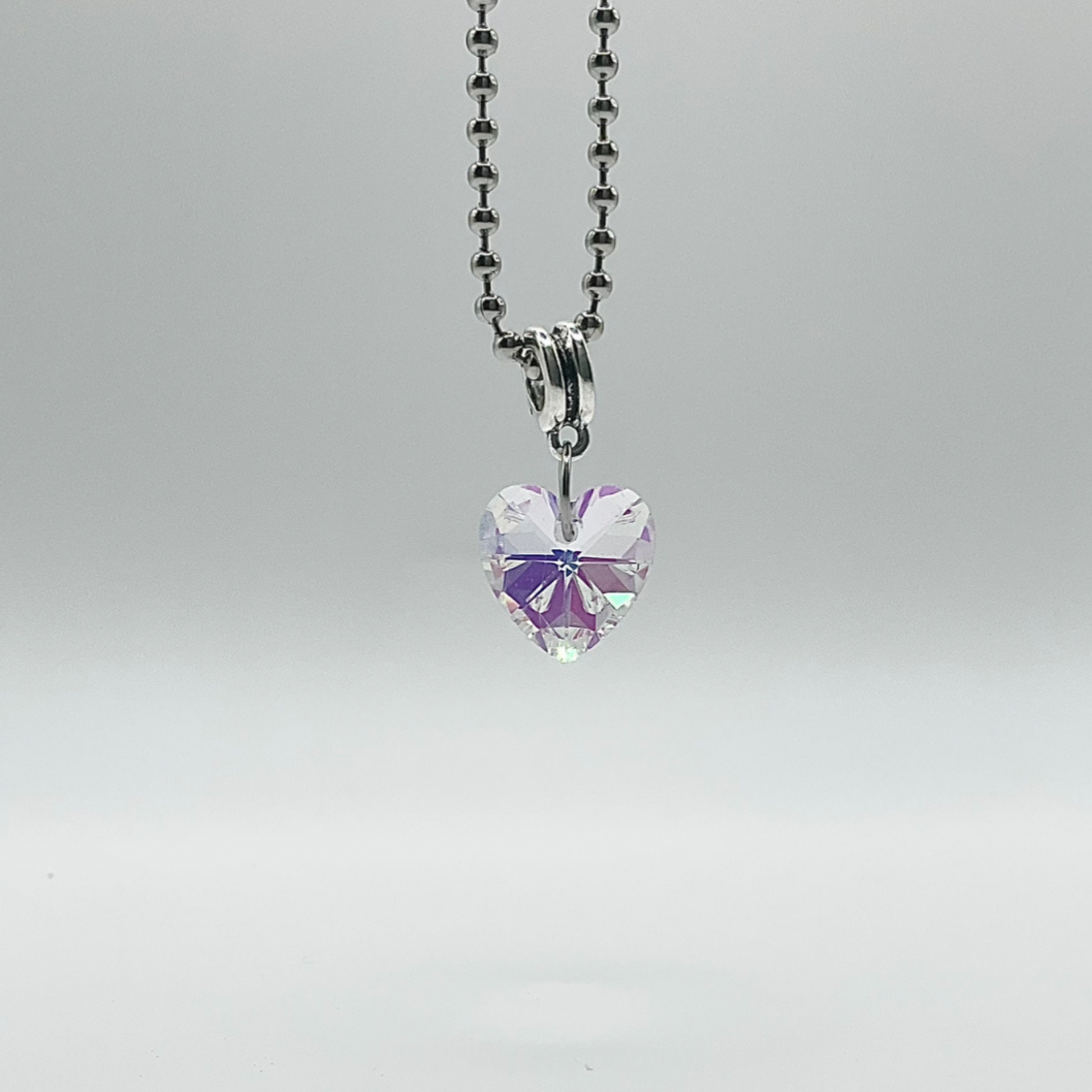 Sparkling Heart-shaped crystal pendant on a ball chain against a gray background