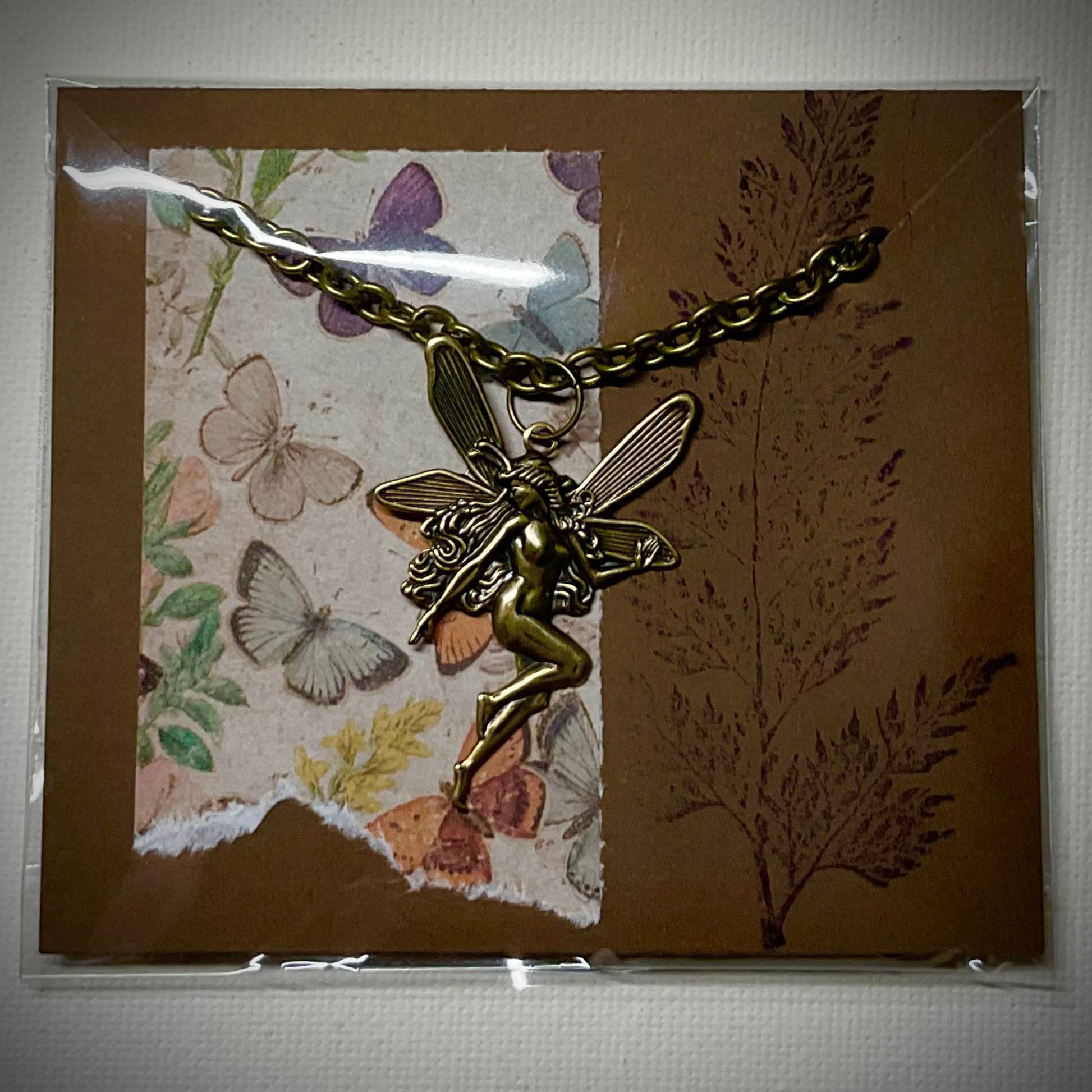 Bronze tone fairy pendant necklace on a decorative card with butterflies and plants
