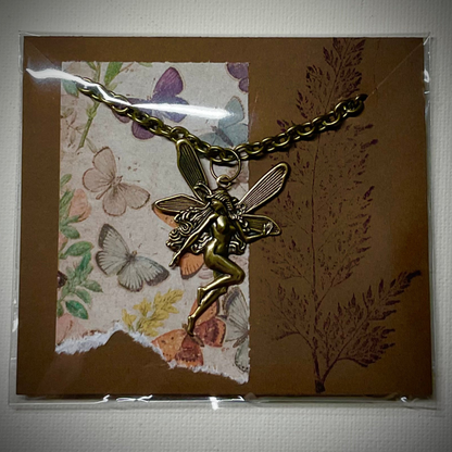 Bronze tone fairy pendant necklace on a decorative card with butterflies and plants
