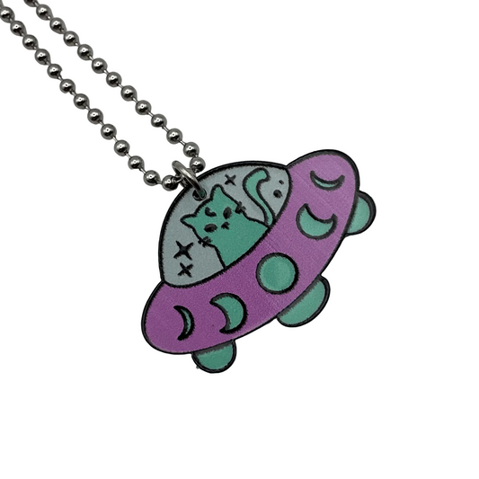Neon pink and green UFO pendant with Kitty occupant on a ball chain against a white background