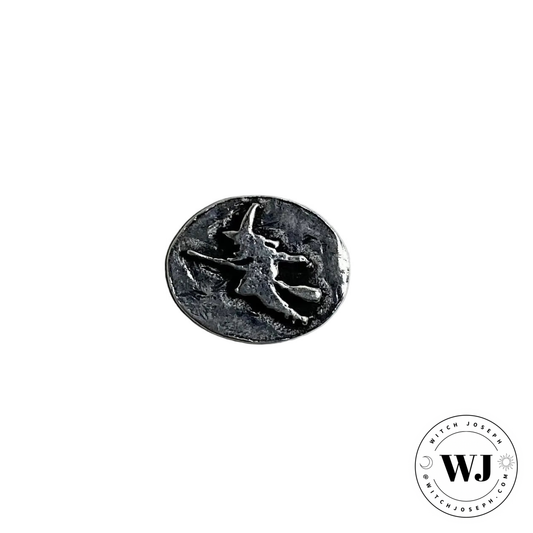 Round metallic charm with flying witch on broom…displayed on a white background, featuring the brand 'WJ'.