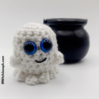 White crocheted ghost with blue eyes and a black cauldron on a white background with the Witch Joseph URL