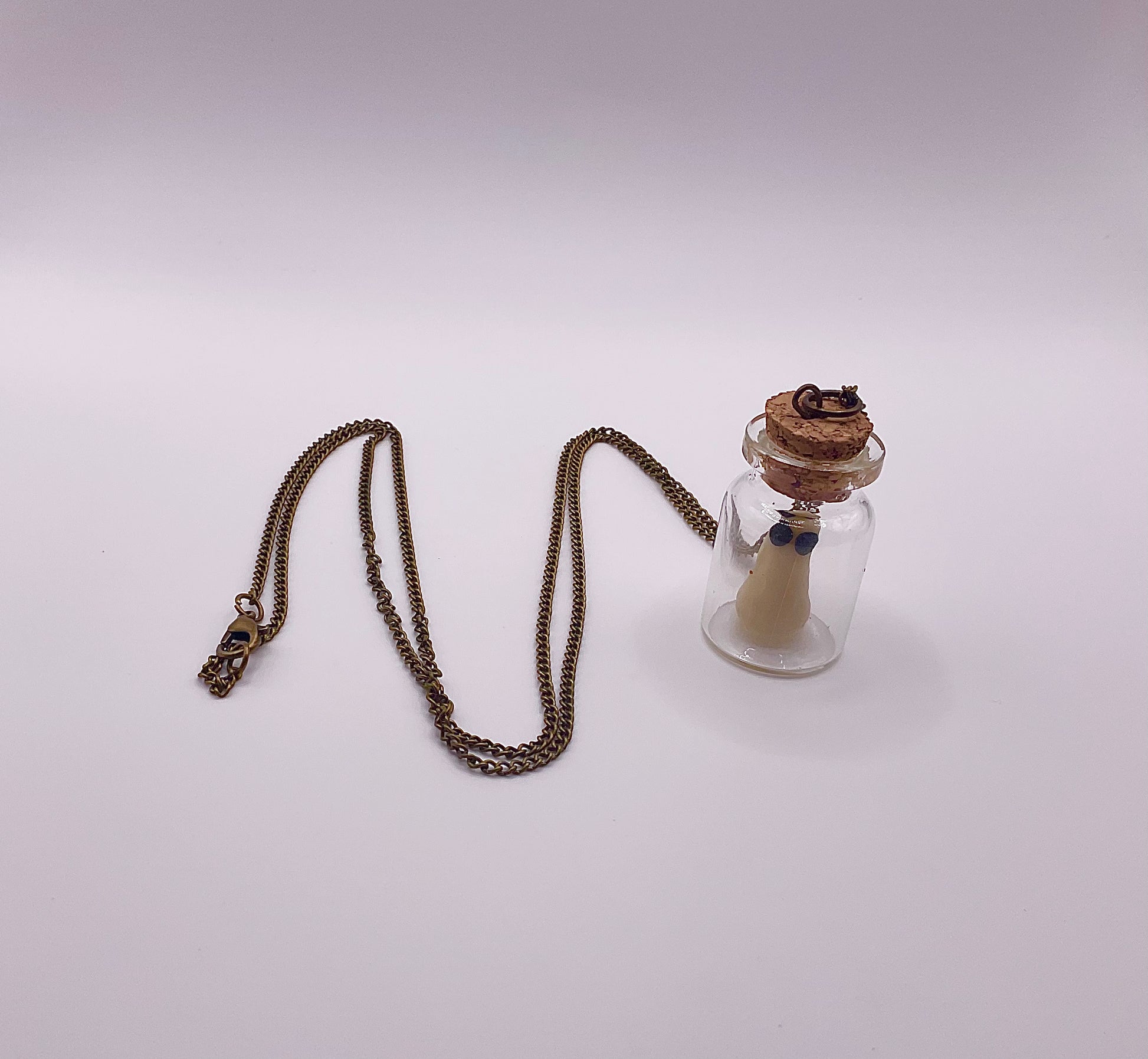 Necklace with a small glass bottle pendant with a small ghost inside displayed on a white background