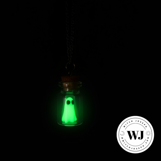 A small glass vial pendant necklace with a cork stopper and a glowing green ghost figure inside, shown against a black background. A circular 'Witch Joseph” brand watermark is visible in the lower right corner.