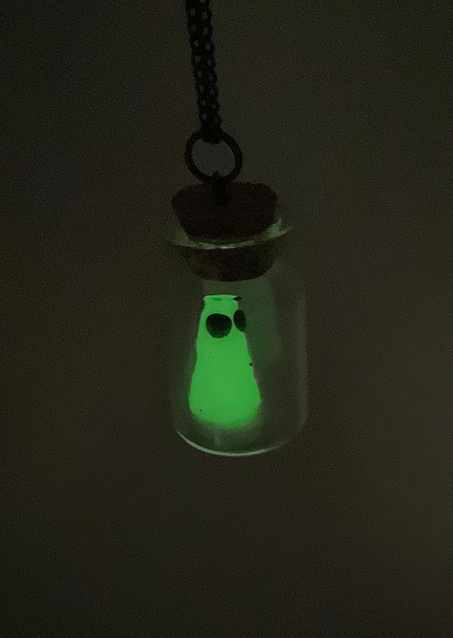 Glowing ghost in a bottle pendant necklace against a dark background