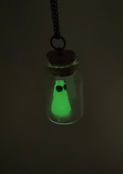 Glowing ghost in a bottle pendant necklace against a dark background