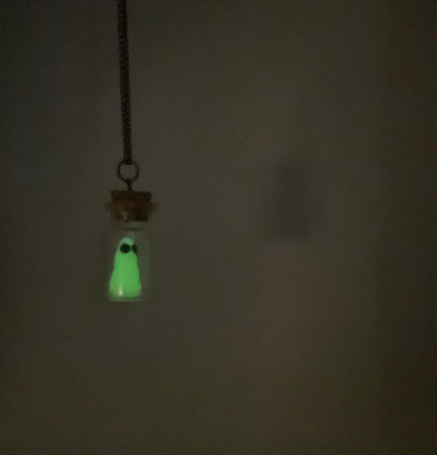 Glowing ghost in a bottle pendant necklace  hanging against a dark background