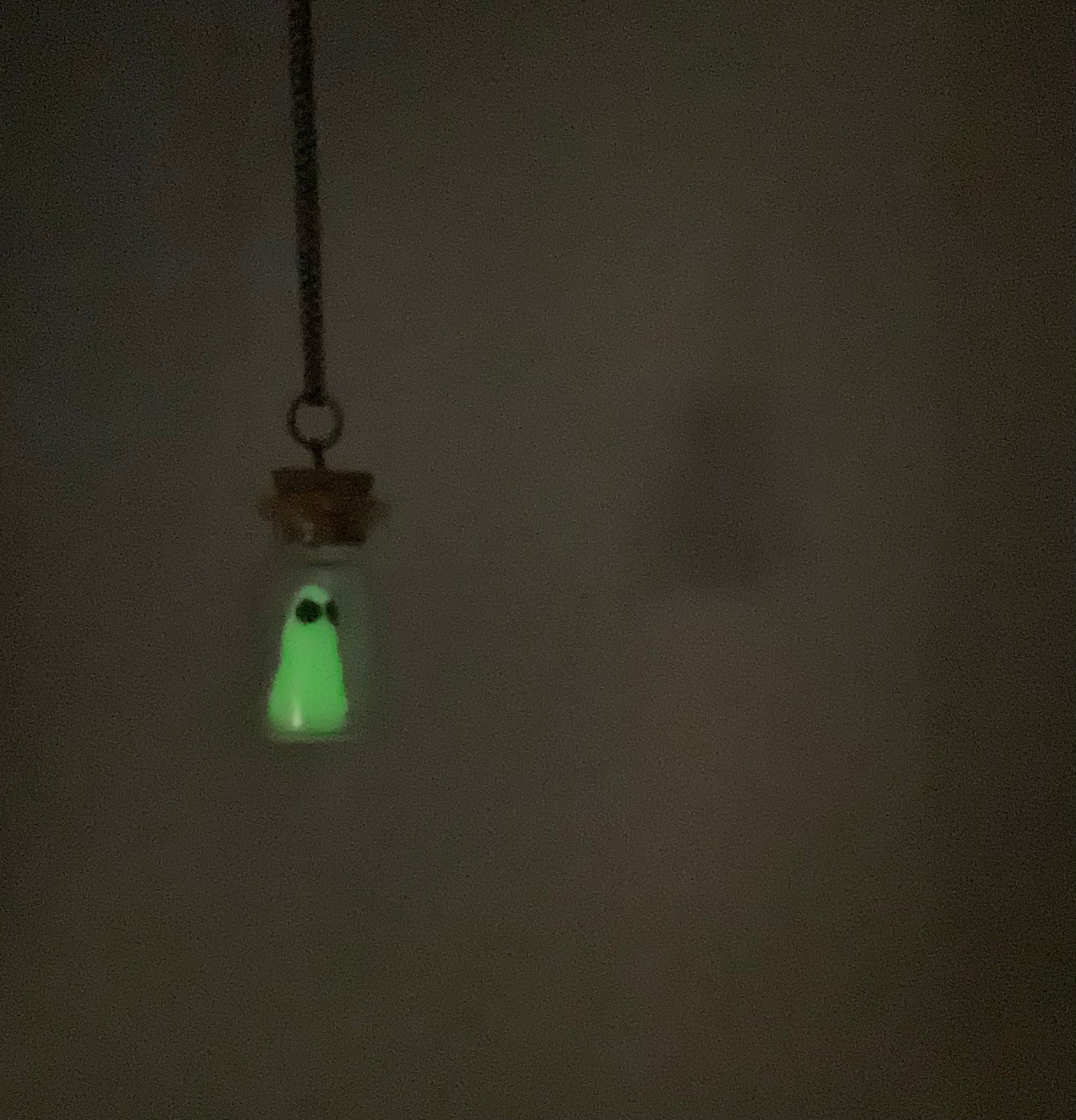 Glowing ghost in a bottle pendant necklace  hanging against a dark background