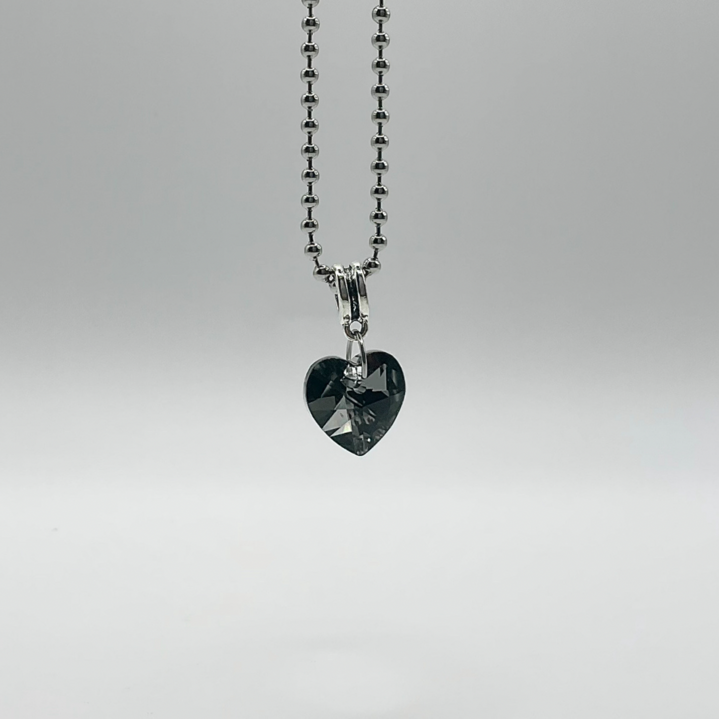 Heart-shaped gray crystal pendant on a silver tone ball chain against a white background