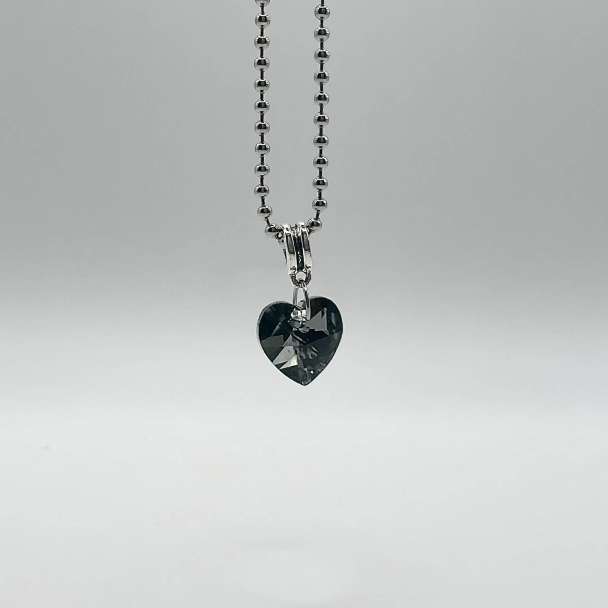 Heart-shaped gray crystal pendant on a silver tone ball chain against a white background