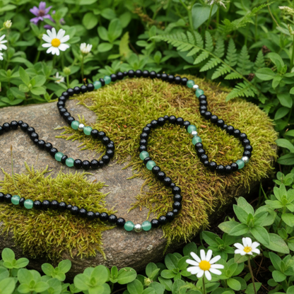 Green Aventurine necklace with black and steel bead accents on a rustic garden rock surrounded by greenery and flowers.