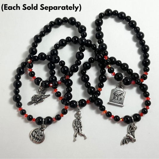 Black beaded stretch bracelets with orange crystal accents with various halloween charms on a white background…with text “each sold separately”