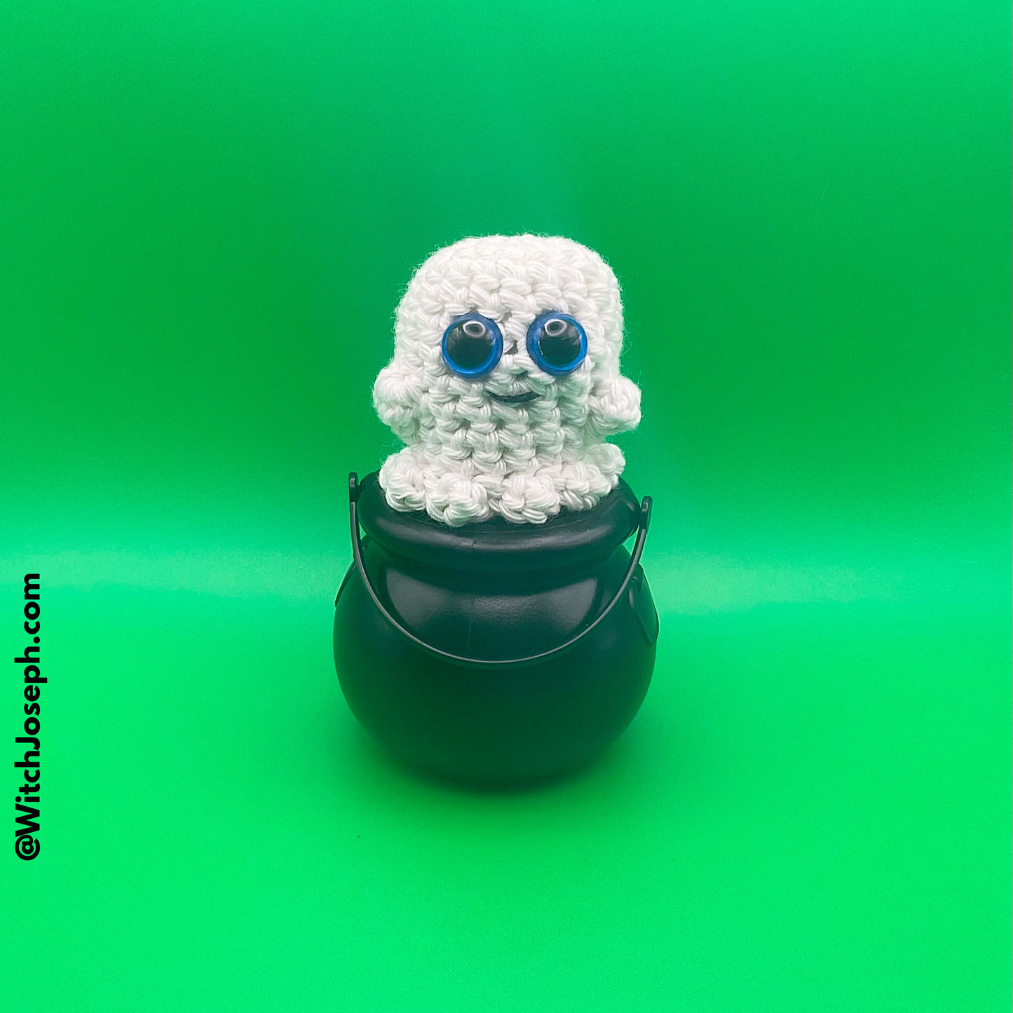 White crochet ghost decoration with blue eyes on a black bucket against a green background with the Witch Joseph URL