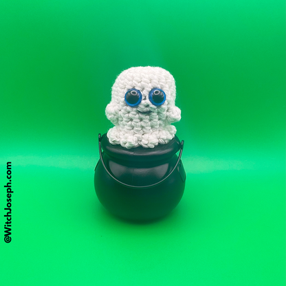 White crochet ghost decoration with blue eyes on a black bucket against a green background with the Witch Joseph URL
