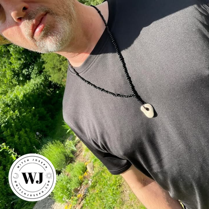 Brother Christopher wearing a black beaded necklace with a Holey stone pendant outdoors in the garden…with the Witch Joseph logo