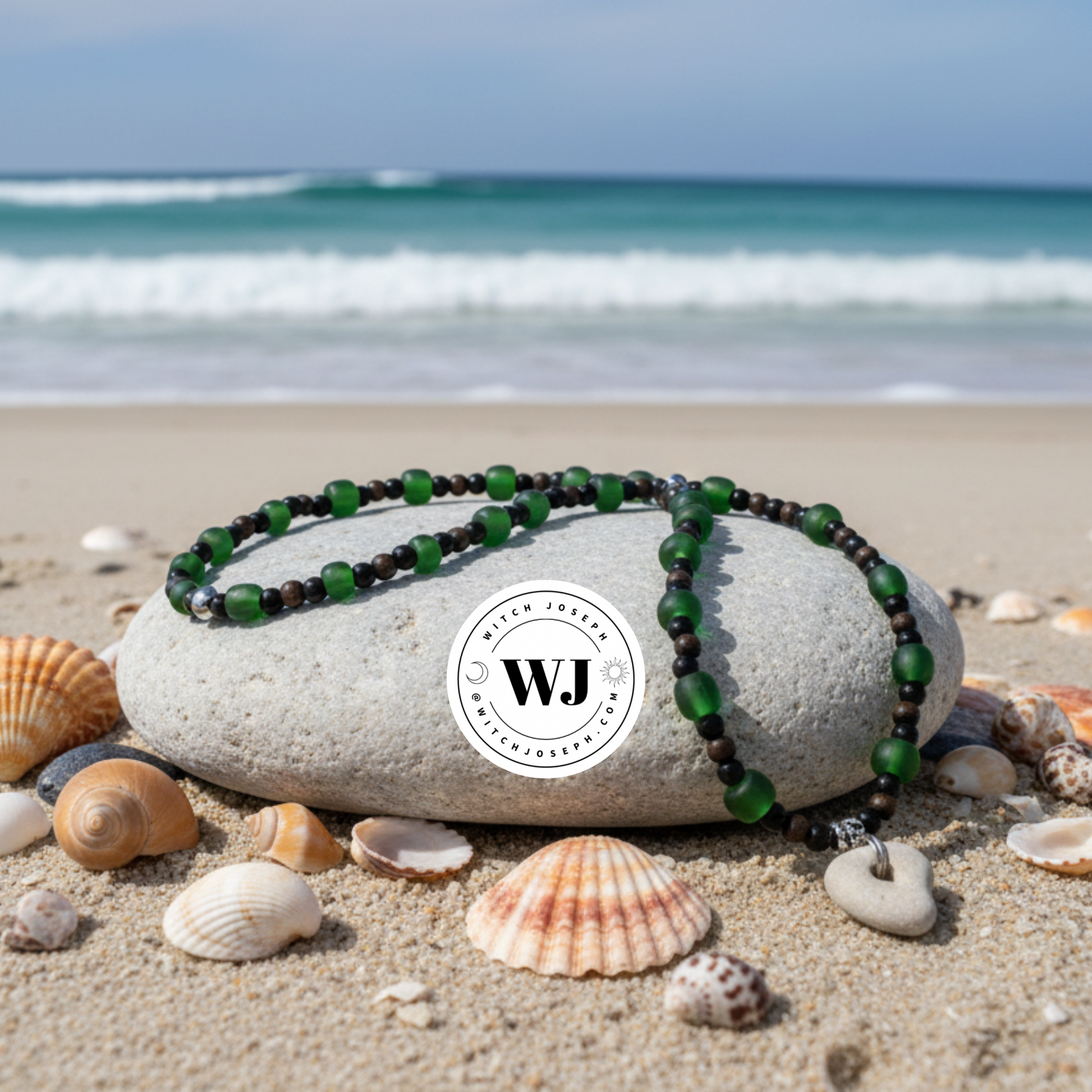 Green beaded necklace with Holey Stone…with green and black and copper accent beads displayed on a rock with seashells and ocean waves in the background, featuring the WJ brand logo.