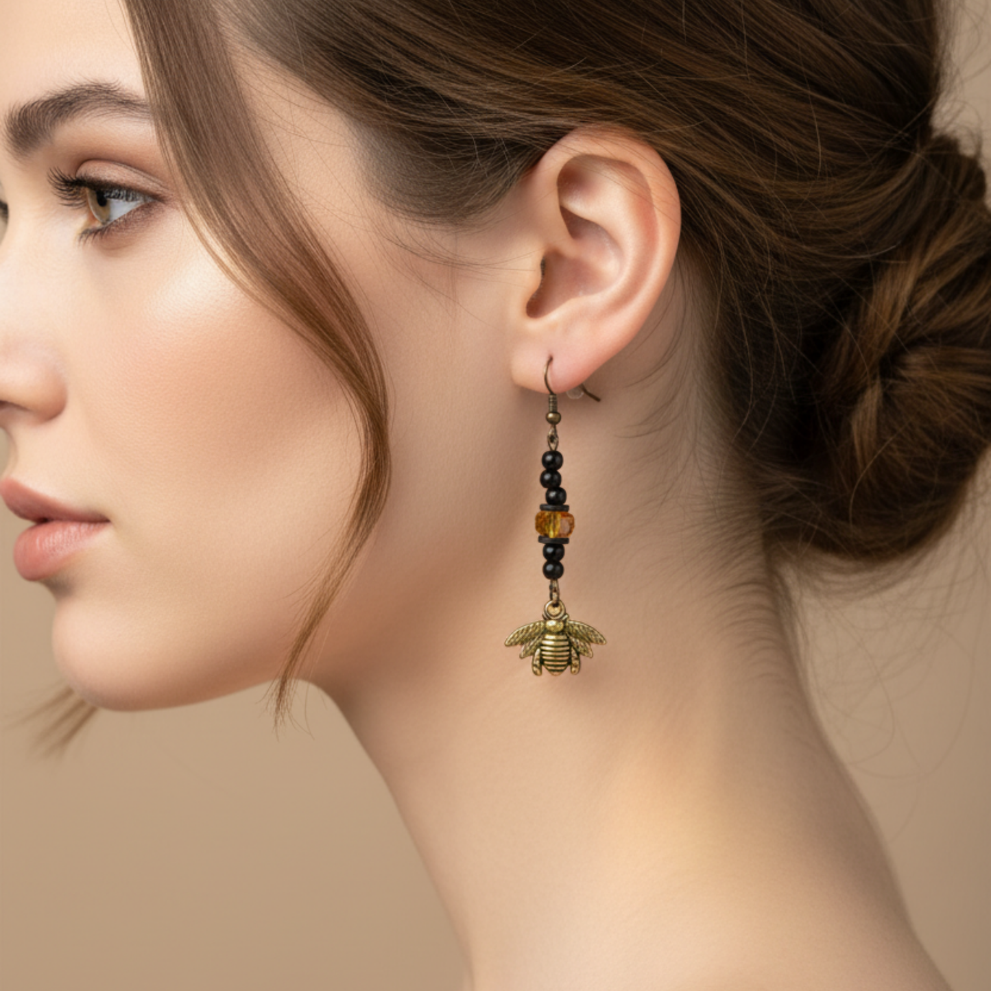Close-up of a woman wearing a bee-shaped earring with black beads and a focal yellow tone sparkle bead against a beige background 