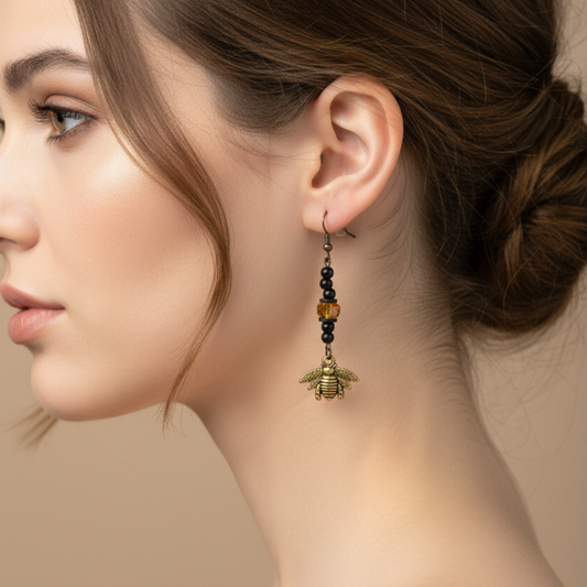 Close-up of a woman wearing a bee-shaped earring with black beads and a focal yellow tone sparkle bead against a beige background 