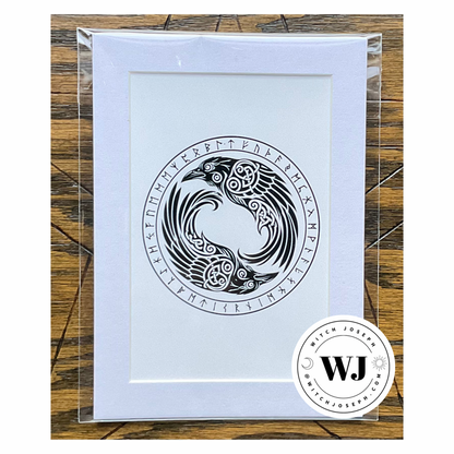 An art print in white mat featuring a black Norse style raven design with runic symbols, enclosed in a clear plastic sleeve and photographed on a wood surface. A circular 'Witch Joseph' logo watermark is visible in the lower right corner.
