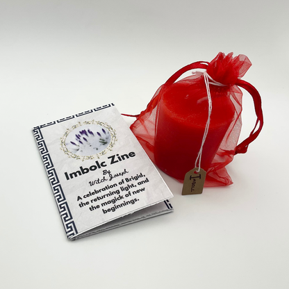 The Imbolc Candle shown in its red organza bag and the Witch Joseph Imbolc Zine, both of which come in the Imbolc Candle lighting kit, shown against a white background.