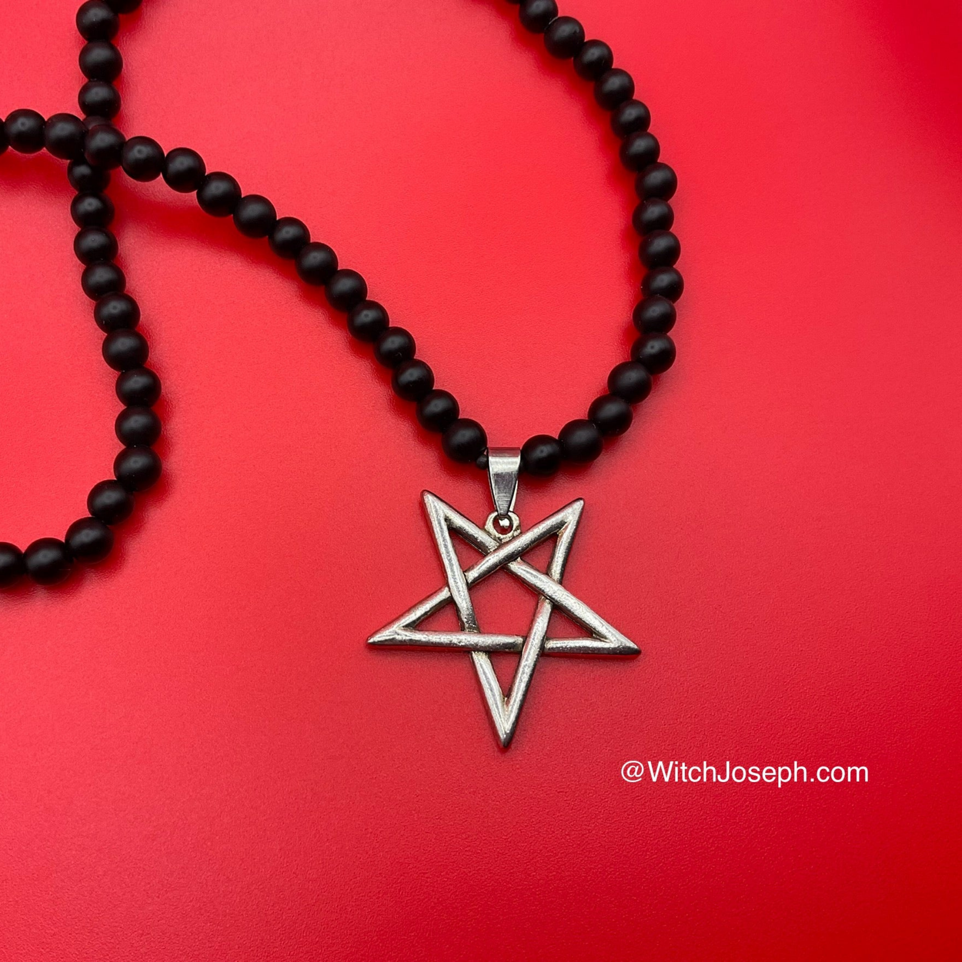 Black beaded necklace with a silver tone inverted pentagram pendant displayed on a red background with the Witch Joseph URL
