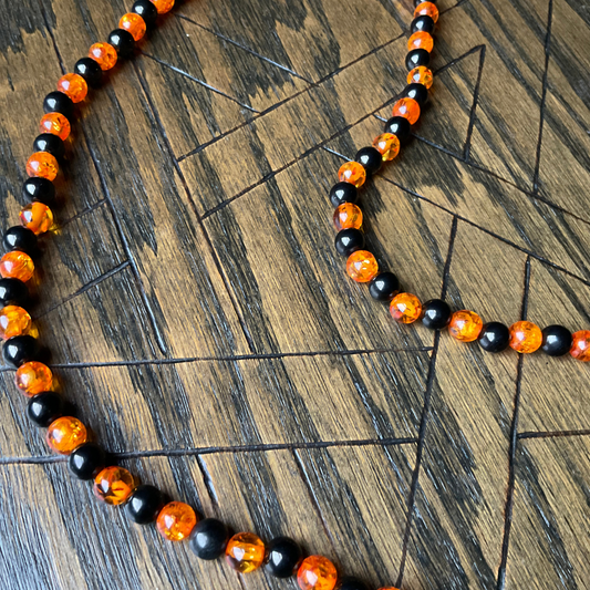 Necklace with large orange and black amber and het beads shown on a wooden surface with an etched Pentagram.