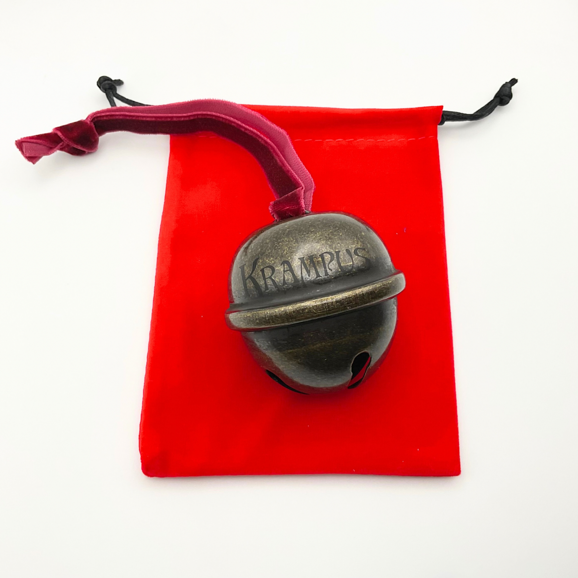 Bronze Krampus bell on a red velvet pouch with black drawstrings.