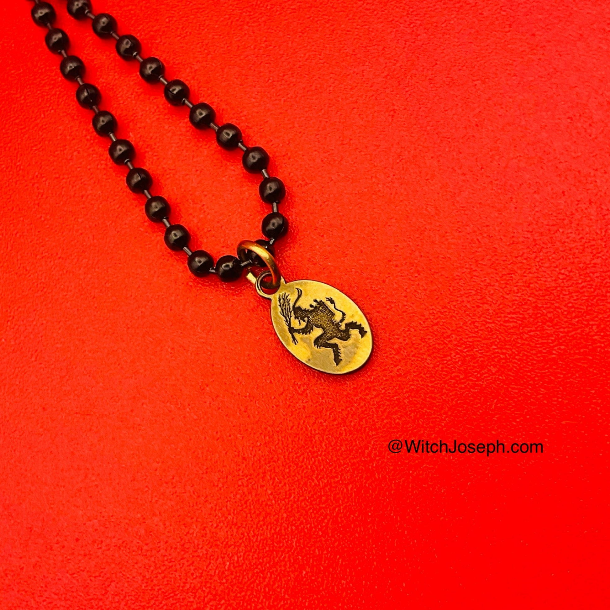 Necklace with a black ball chain and brass Krampus pendant on a red background
