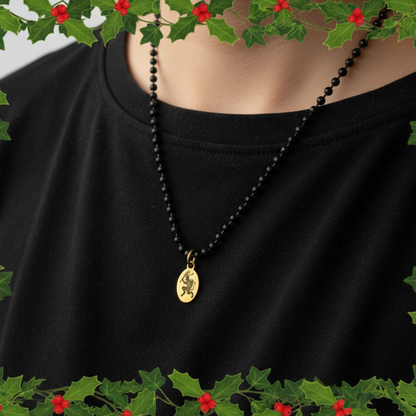 Black ball chain necklace with a brass Krampus pendant on a black shirt, surrounded by holly leaves and berries