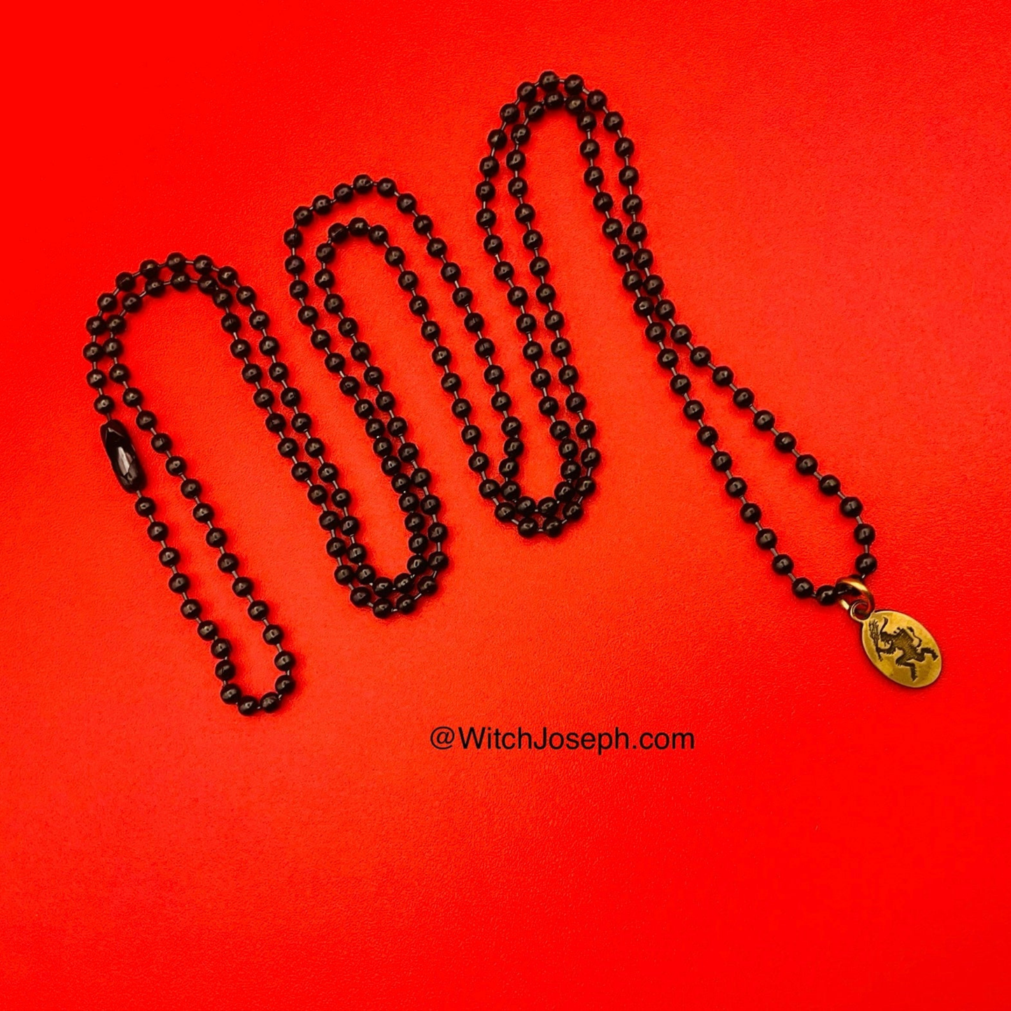Black ball chain necklace with a brass Krampus charm on a red background