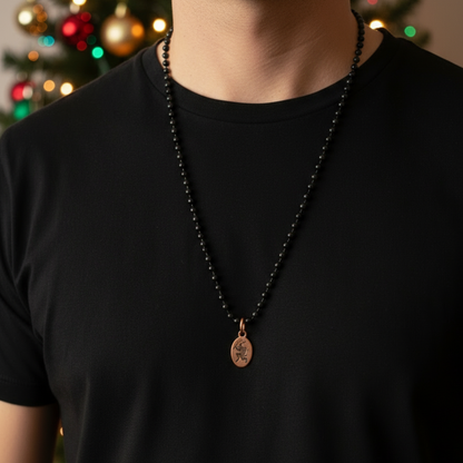 Copper Krampus charm being worn by a person in a black shirt with a Christmas tree in the background