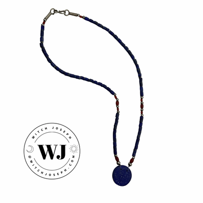 Lapis Lazuli blue beaded necklace, including red and silver tone accent beads,  with a round lapis pendant on a white background, featuring the brand 'Witch Joseph'.