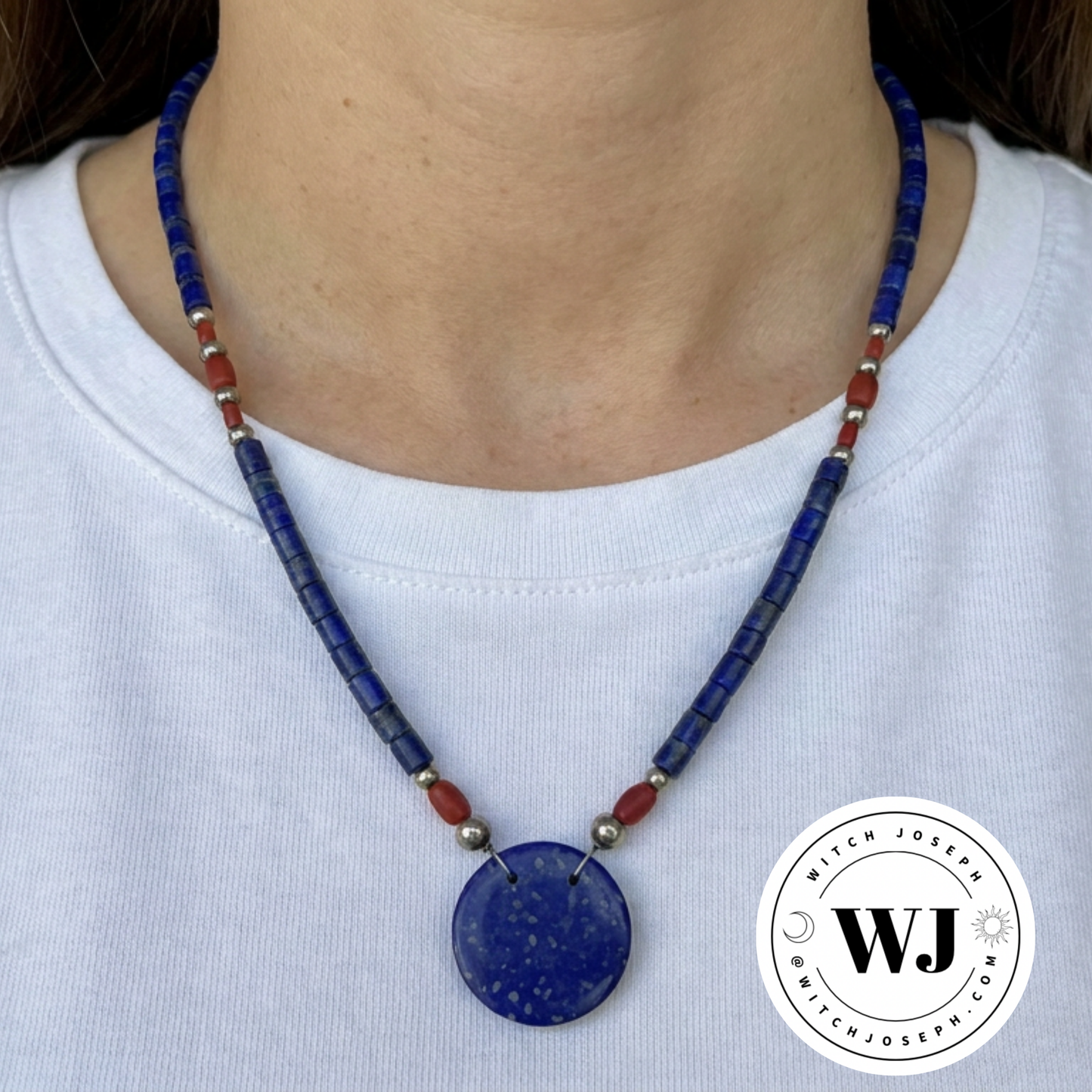 Necklace with blue lapis disc and red and silver tone accent beads displayed  on a white shirt, with a Witch Joseph logo in the corner