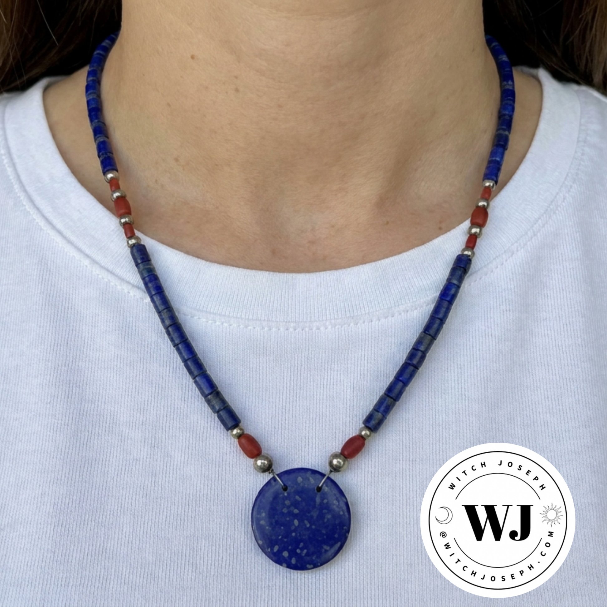 Necklace with blue lapis disc and red and silver tone accent beads displayed  on a white shirt, with a Witch Joseph logo in the corner