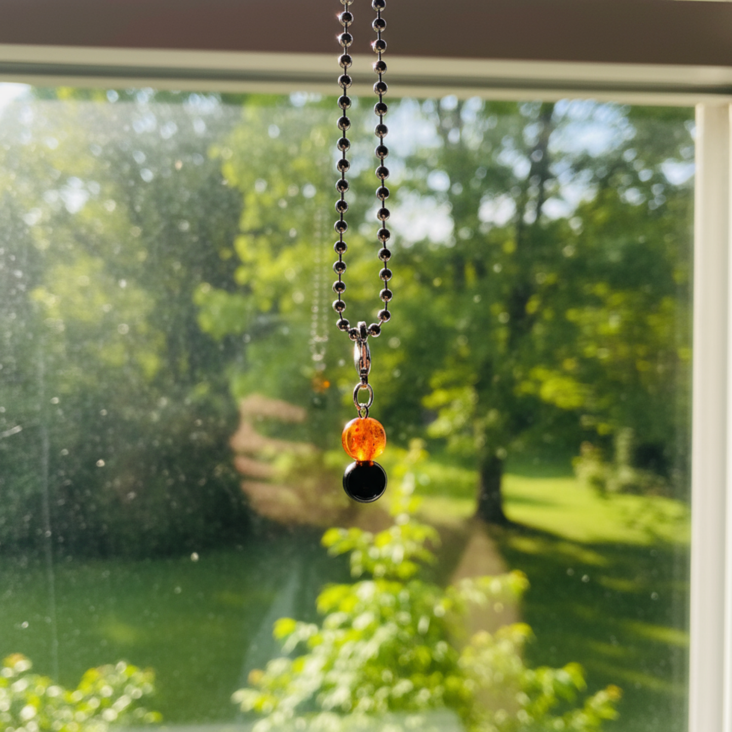 Necklace with amber orange and black jet large bead charm hanging in front of a window with a view of greenery