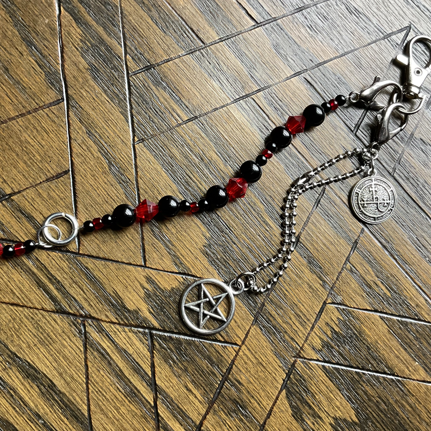 Bag charm with black and red beads and crystals and a pentagram charm and a lilith seal charm displayed on a wooden surface with an etched pentagram