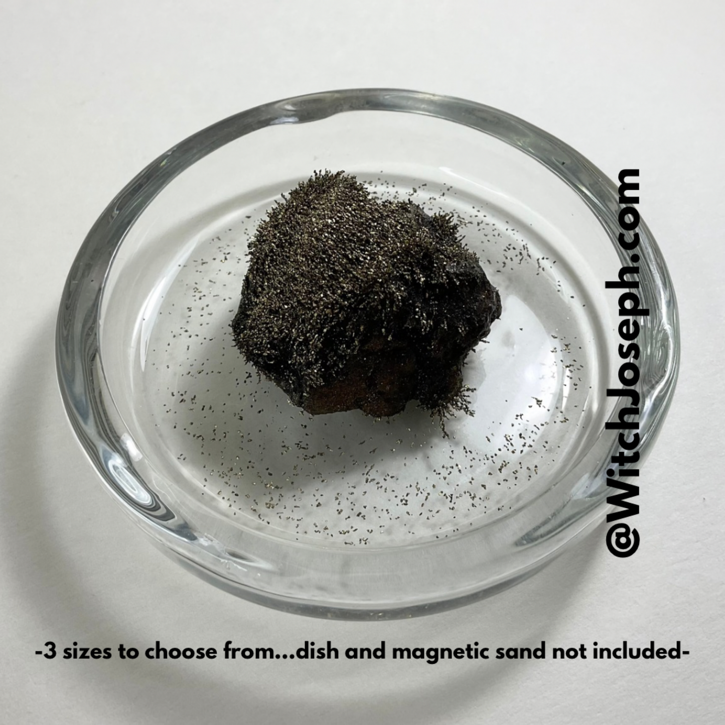 Lodestone in a dish with gold magnetic sand on a white background with the Witch Joseph URL