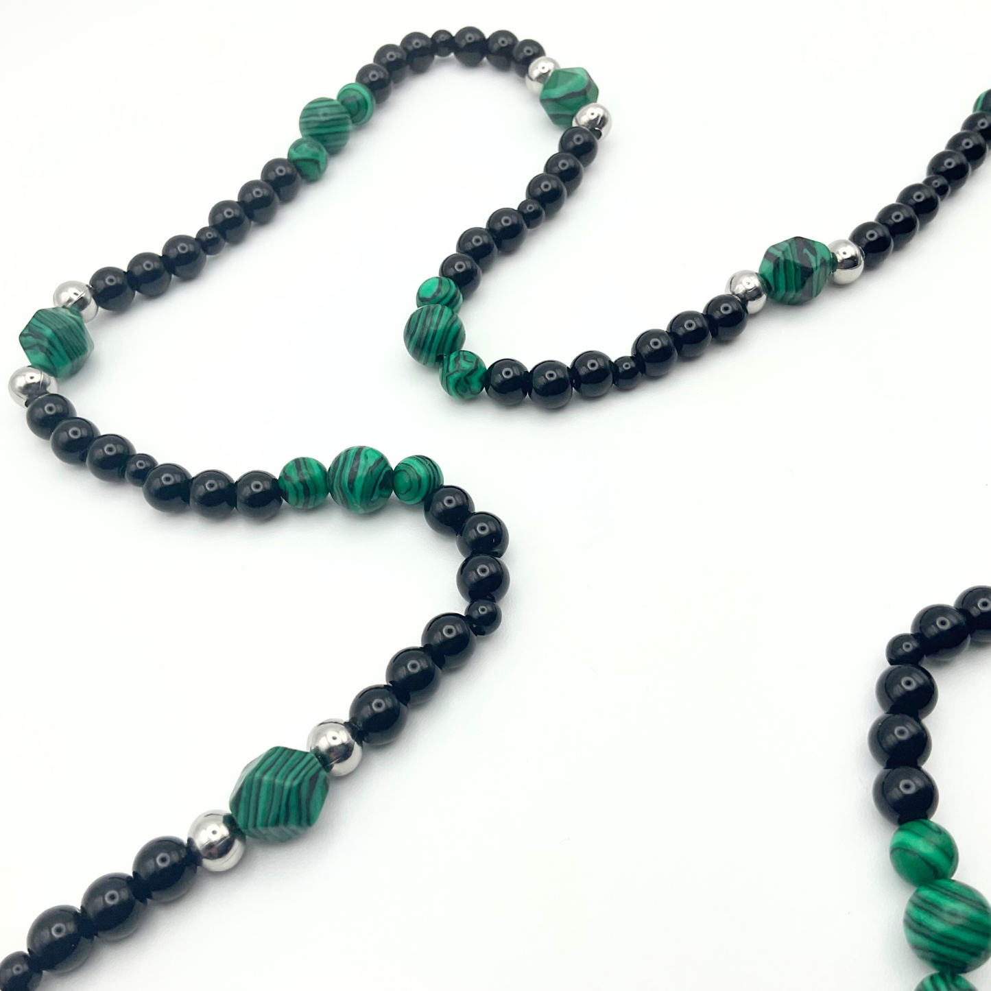 Necklace with green malachite beads and black and steel bead accents on a white background.