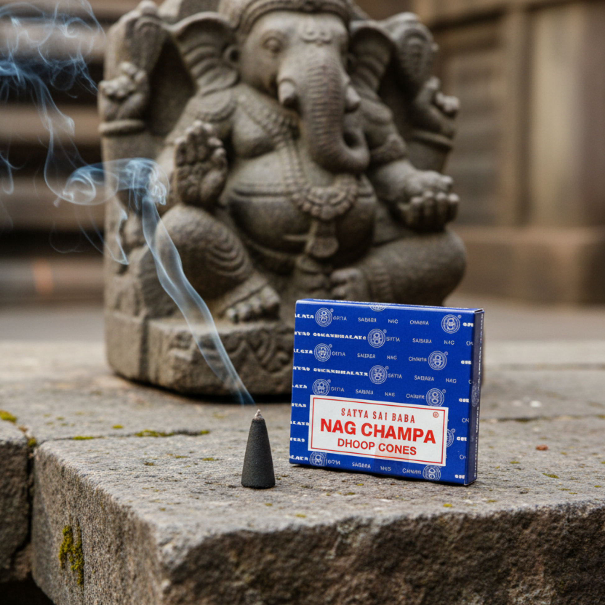 Nag Champa twelve pack dhoop cones package pictured with a smoking incense cone in front of a stone Ganesh statue.