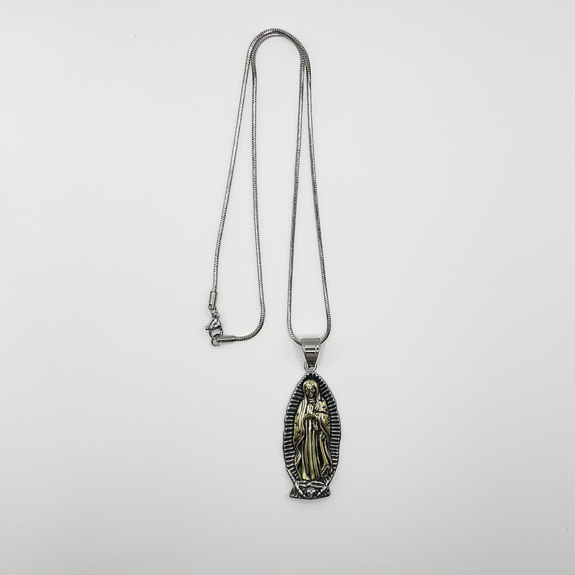 Silver tone necklace with a pendant of our lady of Guadalupe on a silver tone steel chain displayed on a white background