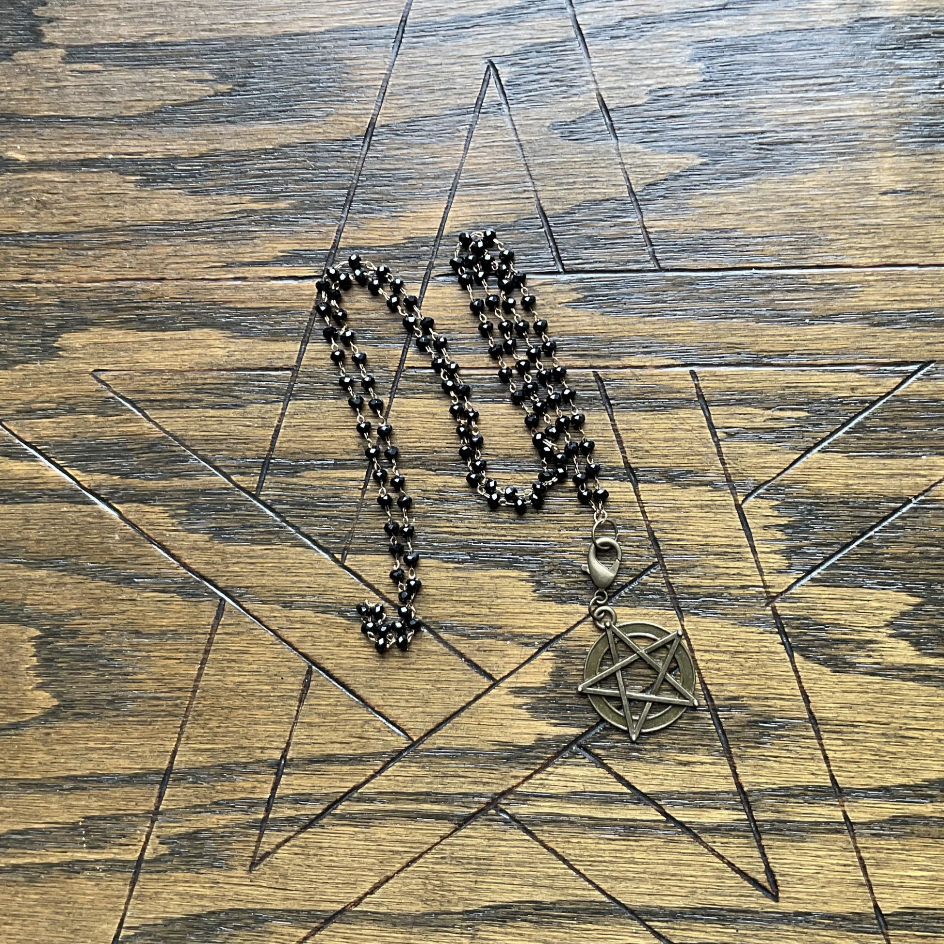 Sparkle bead Necklace with a pentagram pendant displayed on a wooden surface with a pentagram etched onto it