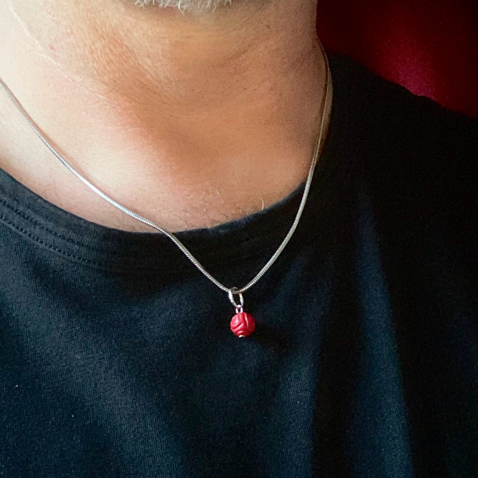 Person wearing a necklace with a rose cu red coral pendant on a plain background