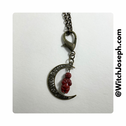 A bronze-toned crescent moon with a red jasper bead pendant, attached to a decorative bronze-toned lobster claw chain.